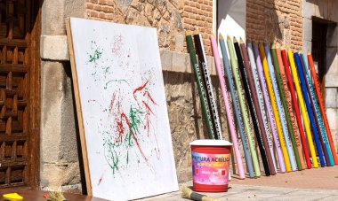 Dev renkli kalemler, dev bir boya tenceresinin yanındaki evin duvarında duruyor ve renkli çizgileri olan bir tuval.