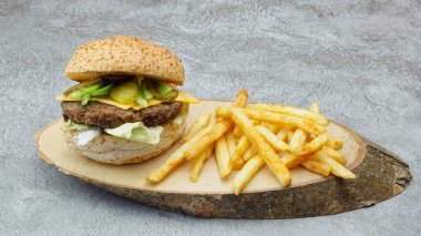 Çedar peynirli lezzetli hamburger, acı biber, Amerikan salatası ve doğal ahşap tepside salatalık turşusu.