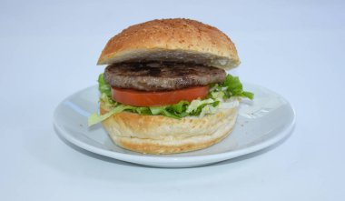 Marul ve domatesli sulu bir hamburgerin yanına beyaz tabak, izole edilmiş fast food.