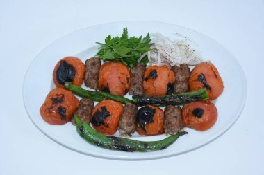 Domates kebabı, bulgur pilavı, kavrulmuş biber, patlıcan ve soğanlı maydanozla servis edilir.. 