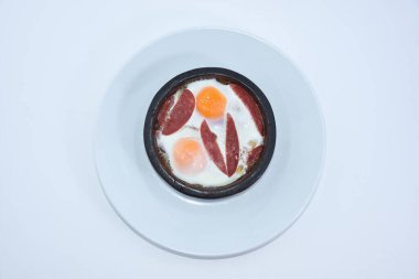 Beyaz tabaklı, güveçte pastırmalı yumurta manzarası.