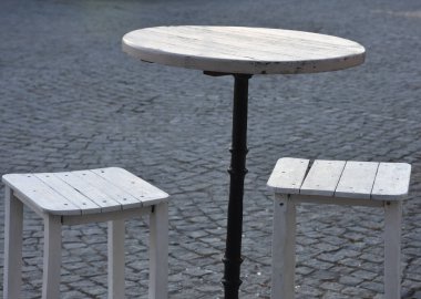 Asfalt bir caddede, bir restoranın önünde küçük bir masa ve taboretler.