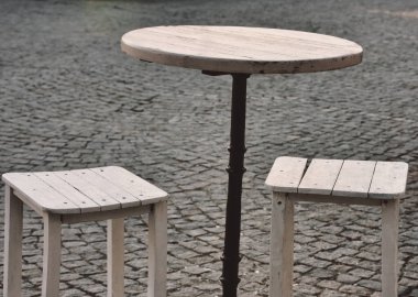 Asfalt bir caddede, bir restoranın önünde küçük bir masa ve taboretler.