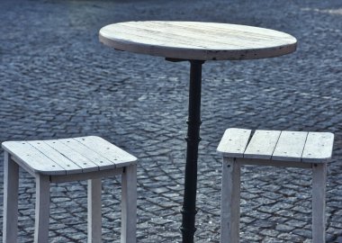 Asfalt bir caddede, bir restoranın önünde küçük bir masa ve taboretler.