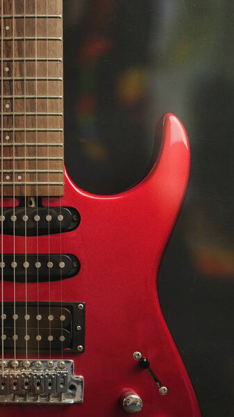 A red shiny electric guitar standing upright on black and bokeh background as wallpaper. Music concept