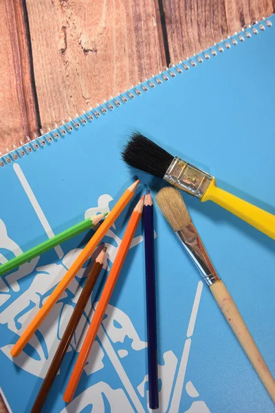 蓝色笔记本上的彩色蜡笔和笔刷 背景为木制 — 图库照片