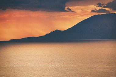 Gökeada 'da deniz üzerinde turuncu gün batımı ve üzerinde Samothrace adasının silueti. Uzak bir Ege adası olan dağlar üzerinden deniz üzerinde gün batımı..