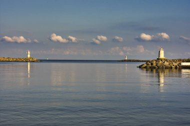 Limanın köşesinde duran eski bir deniz feneri. Dalgalar sorunsuzca sallanıyor. Mavi açık gökyüzü, okyanusun üzerinde kabarık bulutlar.  