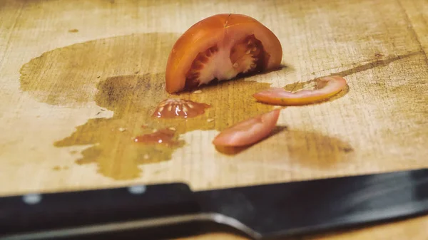 Tomato and knife on a a wooden cutting board.