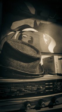 Eski bir amplifikatörün radyo istasyonu ön paneli, modern bir fötr şapka, kitaplar ve yarı görünür soyut bir tablo. Kadıköy, İstanbul, Türkiye 10.13.2022