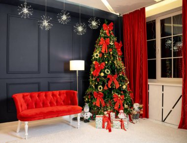 Yeni yıl için dekore edilmiş bir oda. Koyu duvar, kırmızı kanepe, dekorlu Noel ağacı, parlayan lamba, pencere ve perdeler, beyaz halı. Noel ağacının yanında kutular dolusu yay, hediye ve kardan adam var.