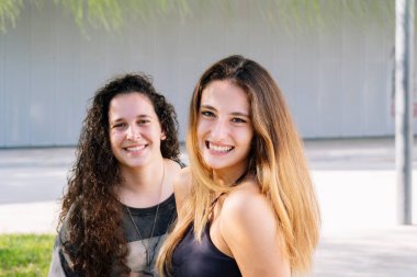 Dışarıda oturmuş kameraya bakan iki kız arkadaş..