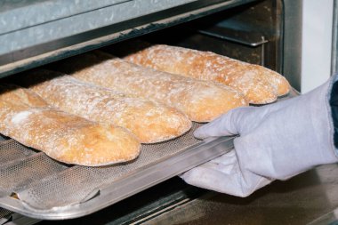 Baker fırından somun ekmeği eldivenle çıkarıyor..