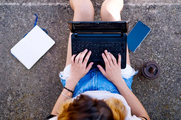 Blonde girl sitting on the floor working with the laptop.
