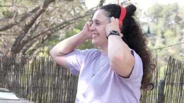 Girl with curly hair listening to music in red headphones.