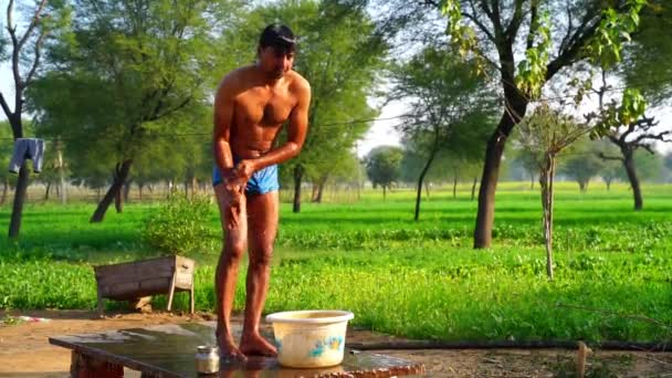 Filmaufnahmen vom frühen Morgen zeigen einen jungen indischen Mann, der mit Plastikeimern im Garten badet. Zeitlupenaufnahmen. — Stockvideo