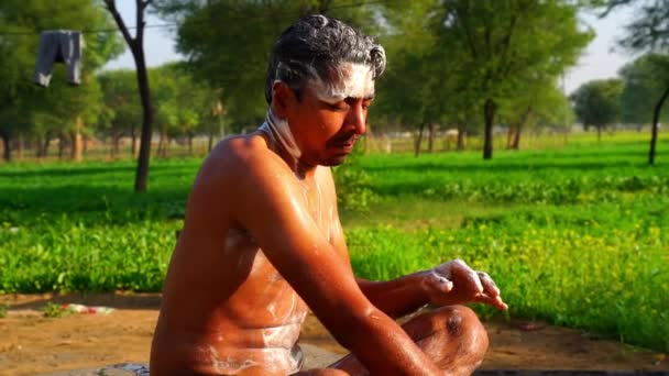 Joven hombre indio bañándose con cubo en medio del campo en la naturaleza. Imágenes del pueblo rural indio. Vídeo en cámara lenta — Vídeos de Stock