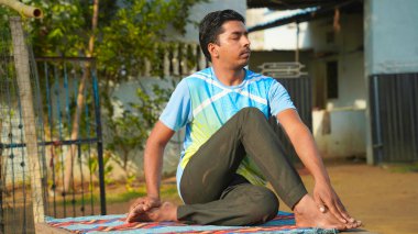 Genç yakışıklı adam yoga yapıyor, balıkların yarı lordu egzersizi yapıyor. Spor kıyafetleri, pantolonlar ve tişörtler..