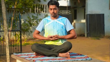 Genç sporcu yoga yapıyor, Sukhasana egzersizi yapıyor. Siyah pantolon ve mavi gömlek, kapalı mekan, yoga stüdyosu.