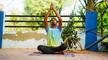 Spor kıyafetleri giyen, meditasyon yapan, nefes alan, bacak bacak bacak üstüne atmış genç bir adam..