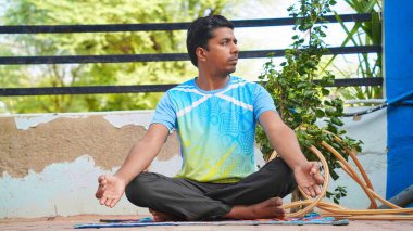 Genç Hintli adam güneş doğarken yoga minderinin üzerinde nilüfer pozisyonunda oturuyor.