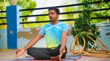 Genç Hintli adam güneş doğarken yoga minderinin üzerinde nilüfer pozisyonunda oturuyor.