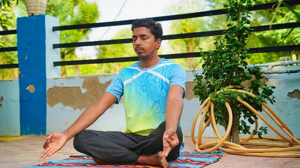 Genç Hintli adam güneş doğarken yoga minderinin üzerinde nilüfer pozisyonunda oturuyor.