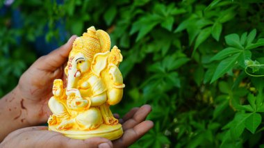 Eco friendly Ganesh or Ganpati idol or murti in hand with nature background, home made. selective focus. Ganesha chaturthi festival 2022.