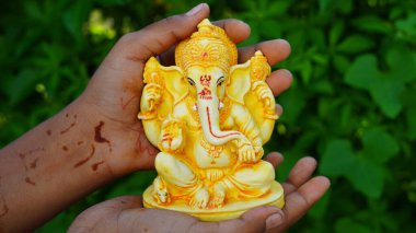 Eco friendly Ganesh or Ganpati idol or murti in hand with nature background, home made. selective focus. Ganesha chaturthi festival 2022.