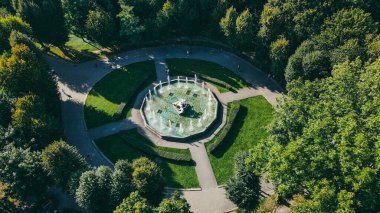 İnsanlar yazın parktaki meydanda taş çeşmenin etrafında yürürler.