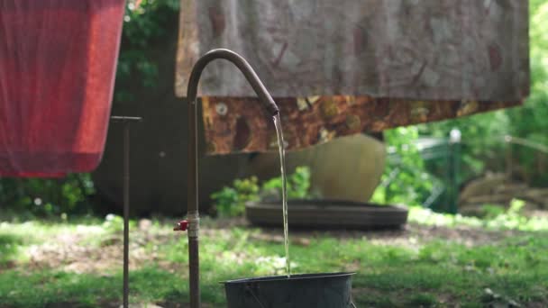 El agua corriente fluye en un cubo en el patio del jardín. Sacar agua de un pozo — Vídeos de Stock