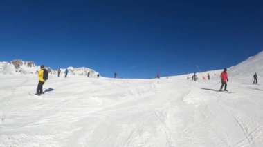 Turuncu takım elbiseli bir snowboardcu yamaçtan aşağı iniyor.