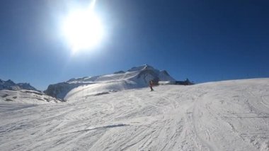 Turuncu takım elbiseli bir snowboardcu yamaçtan aşağı iniyor.