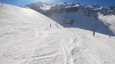 Turuncu takım elbiseli bir snowboardcu yamaçtan aşağı iniyor.