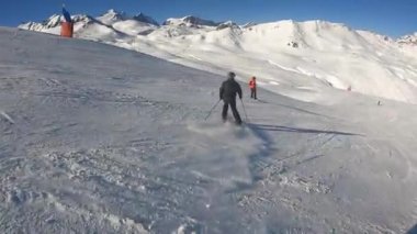 Turuncu takım elbiseli bir snowboardcu yamaçtan aşağı iniyor.