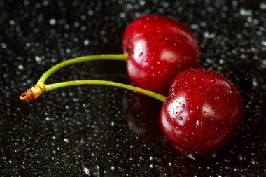 İki lezzetli olgun kiraz siyah yansıtıcı zemin su ile makro çekim bırakır. Sığ derinlik-in tarla