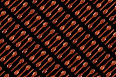 Koyu tahta kaşıklardan yapılmış desen, zıt yönlere yerleştirilmiş, siyah üzerine izole edilmiş. Üst görünüm, düz uzanan minimalist arkaplan