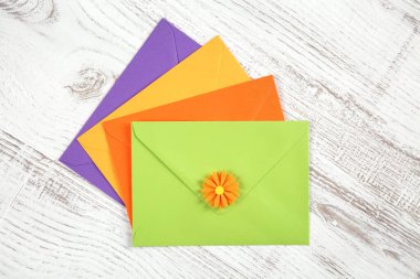 Geri dönüştürülmüş kağıttan dört renkli zarfın ve kırsal beyaz bir masa üzerindeki dekoratif çiçeğin üst görüntüsü.