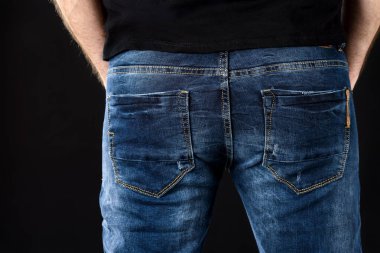 Close up of a fit and sexy male butt in classic blue jeans and black t-shirt against black background. Men's casual fashion clothing