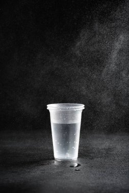 Donmuş hareket plastik bardakların üzerine su püskürterek siyah zemin üzerinde su damlaları oluşturur.