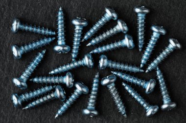 Aşırı yakın çekim, yukarıdan aşağıya mavi renkli, paslanmaz çelik, küçük, tencere başlı vidalar siyah taş yüzeyde.
