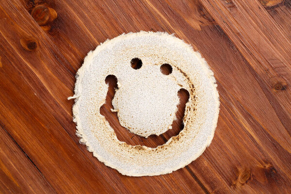 Top down view of an used, round sandpaper disk, looking like a smiling face, on a dark wood surface. Eco friendly industrial concept.