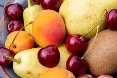 Bir kasede armut, kiraz, kayısı ve kivi.