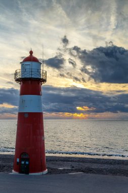Sahildeki güzel kırmızı ve beyaz deniz fenerinin manzaralı görüntüsü.