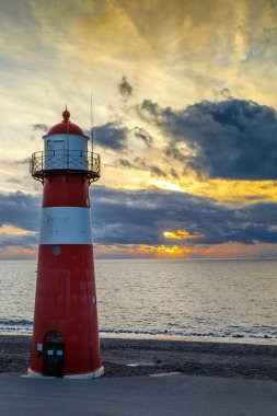 Sahildeki güzel kırmızı ve beyaz deniz fenerinin manzaralı görüntüsü.