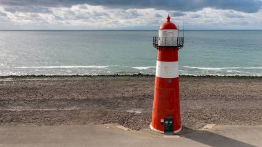 Sahildeki güzel kırmızı ve beyaz deniz fenerinin manzaralı görüntüsü.