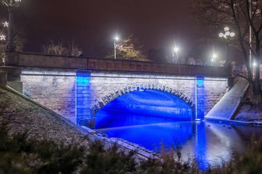 Riga 'daki Bastion Hill şehir parkında (Letonya) Alexander Köprüsü' nün gece manzarası. Köprü 1858-1859 yılları arasında inşa edildi ve 1902 yılında genişletildi..