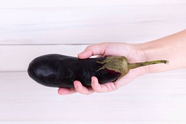 Beyaz ahşap arka planda insan elinde mor patlıcan..