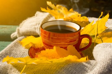 Bir fincan kahve, sonbahar akçaağaç yaprağı, ahşap bir arka planda eşarp.