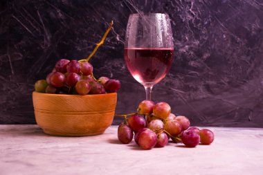 Kırmızı şarap kadehi, beton zeminde taze üzümler.